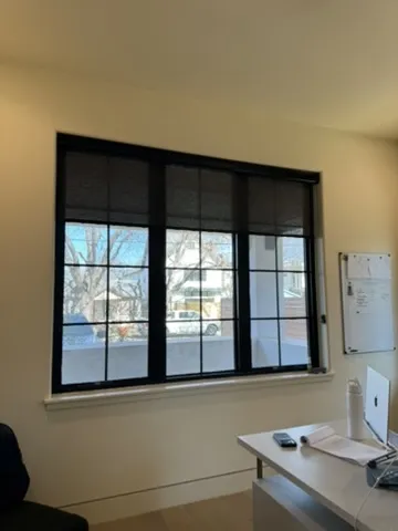 Textured light-filtering roller shades installed on large black-framed office window in Tarrytown Austin home with white desk.