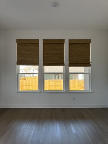Natural woven shades installed in a Kyle, TX bedroom with three large windows, providing privacy, light control, and warm textured design.