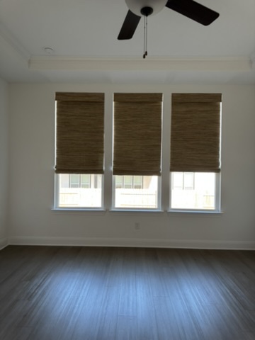 Custom natural woven shades in a Kyle, TX bedroom with three windows, adding texture, privacy, and soft filtered light.