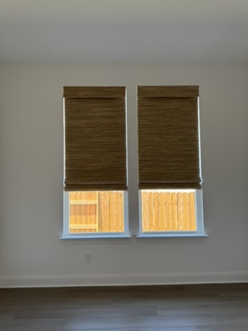 Custom natural woven shades in a Kyle, TX bedroom with two large windows, offering privacy, filtered light, and a warm natural look.