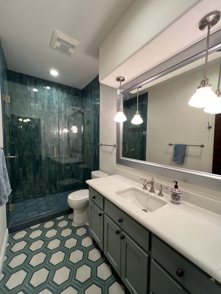Georgetown bathroom featuring a glass walk-in shower with rich green tile, hexagon flooring, and a clean vanity with polished finishes.