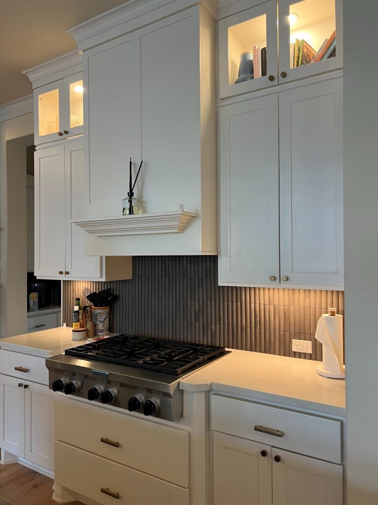 Georgetown kitchen with white cabinetry, brass hardware, built-in range hood, and vertical tile backsplash.