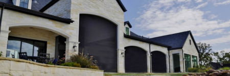 Motorized exterior shades installed across arched patio openings on a luxury stone home in Austin.