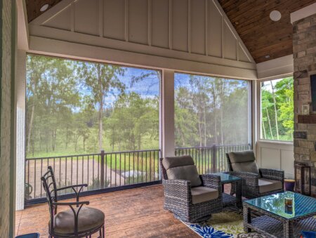 Exterior shades on a covered Austin patio with outdoor lounge chairs, stone fireplace, and wooded backyard view.