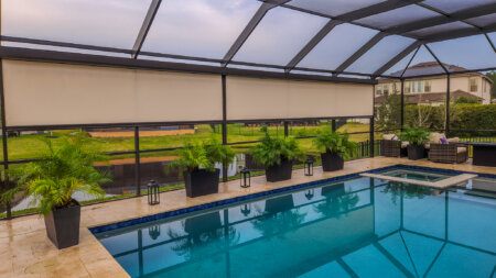 Exterior shades on an Austin pool enclosure with potted palms, covered lounge seating, and a backyard water view.
