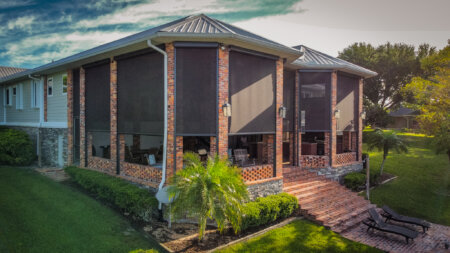 Exterior shades on a brick Austin home with a covered patio, palm trees, outdoor seating, and lawn views.