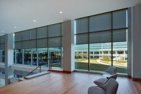 Hunter Douglas solar shades on tall commercial lobby windows with modern seating.