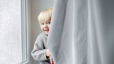 toddler hiding behind a window covering