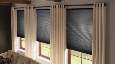 living room with 3 windows with honeycomb/ cellular shades in a black light filtering shade, along with drapery