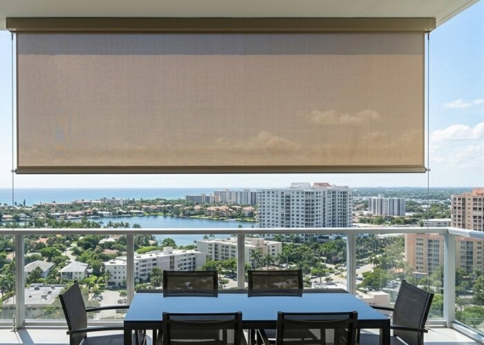 Minimalist cable-guided outdoor solar shade in a sand-colored fabric installed on a high-rise Boca Raton balcony, featuring discreet stainless steel cables and a view of the Florida coastline.